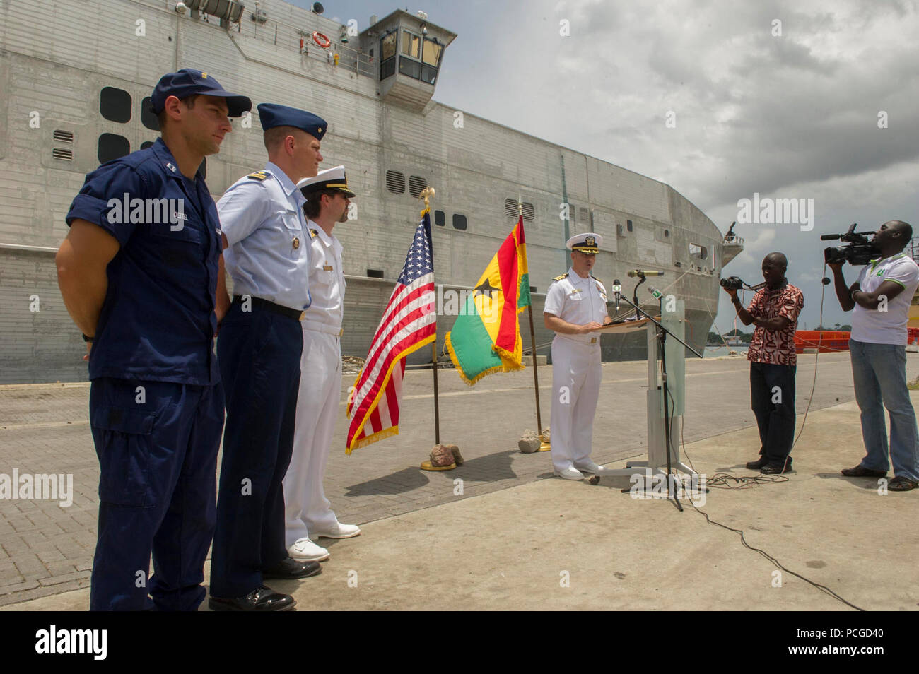 Ghana (11 avril 2014) U.S. Coast Guard Le Lieutenant Jeffrey Deitel, gauche, détachement de l'application de la loi responsable de la Garde côtière des États-Unis, le lieutenant Cmdr. John Carter, l'application du droit maritime de l'Afrique Société de l'agent responsable de l'établissement, et le Capitaine Doug Casavant, civil service maître du transport maritime militaire conjointe commande bateau à grande vitesse l'USNS Lance (JHSV 1), regard sur la marine américaine comme le Capt Marc Lederer, commandant de la mission de Spearhead, donne un discours lors de la cérémonie de clôture pour le partenariat pour l'application du droit maritime. Le partenariat est la phase opérationnelle de l'Afrique centrale et de partenariat rassemble Banque D'Images