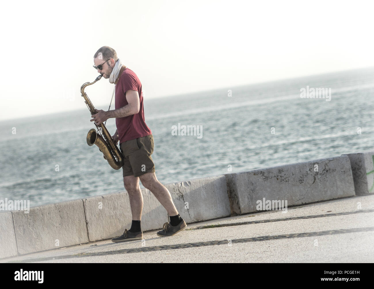 Musicien de rue jouant du saxophone sur la promenade du front de mer de Lisbonne avec vue sur le fleuve Tage, Portugal - représentation décontractée au bord de la rivière Banque D'Images