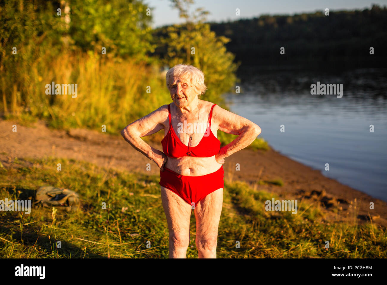 Une femme âgée dans un maillot de bain est sur la rive du fleuve. Banque D'Images