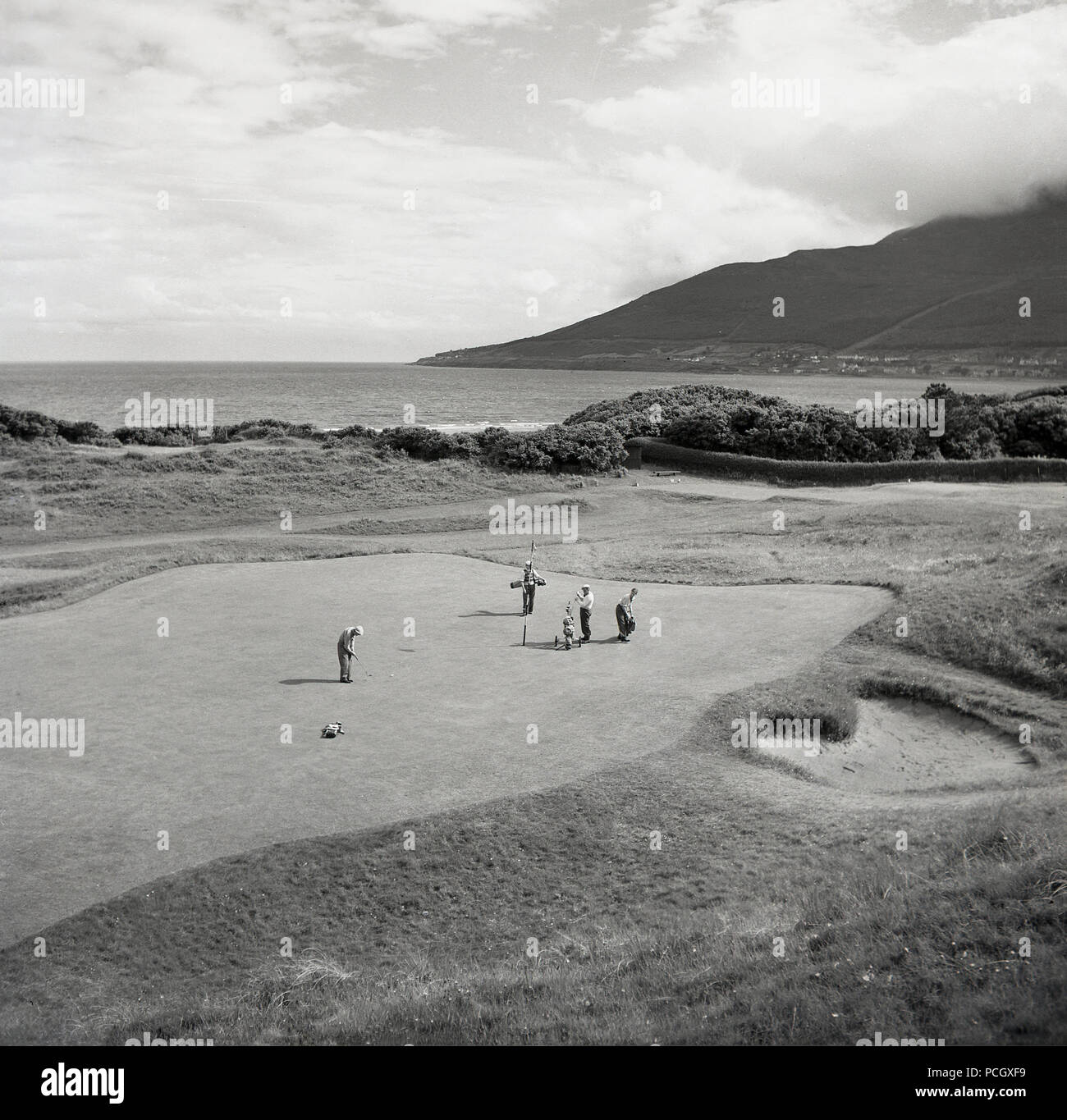 Années 1950, historique, vue de dessus du golf sur le parcours de Portrush dans Co. d'Antrim, en Irlande du Nord. Les golfeurs d'Amateur sur un grand putting green par la côte sur l'océan Atlantique. Banque D'Images