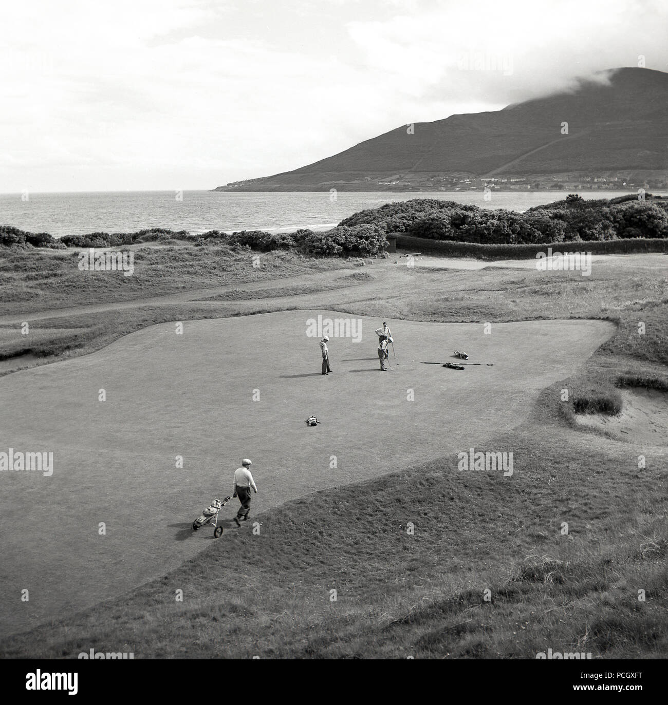 Années 1950, historique, du golf sur un parcours en liens Co. d'Antrim, en Irlande du Nord. Les golfeurs d'Amateur sur un grand putting green par la côte sur l'océan Atlantique. Banque D'Images