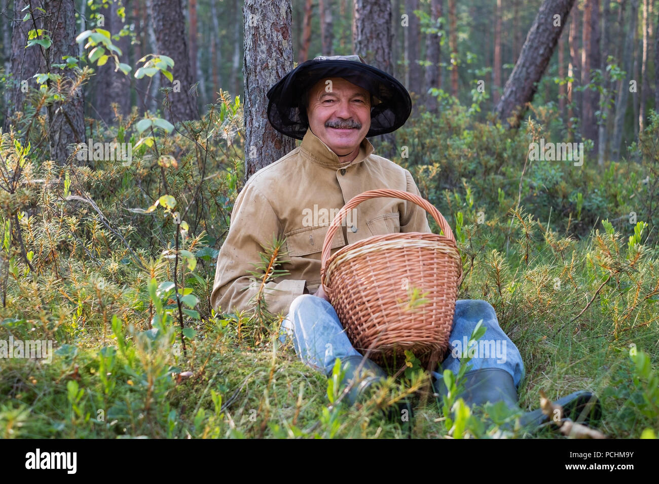 Portrait de relaxed mature homme assis dans la forêt avec panier. Banque D'Images