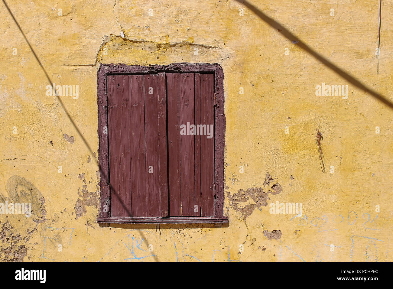 La couleur jaune de l'essuyé une façade de maison à El Jadida, Maroc. Fenêtre avec un obturateur fermé brun en bois. Les lignes d'ombre des câbles dans le st Banque D'Images