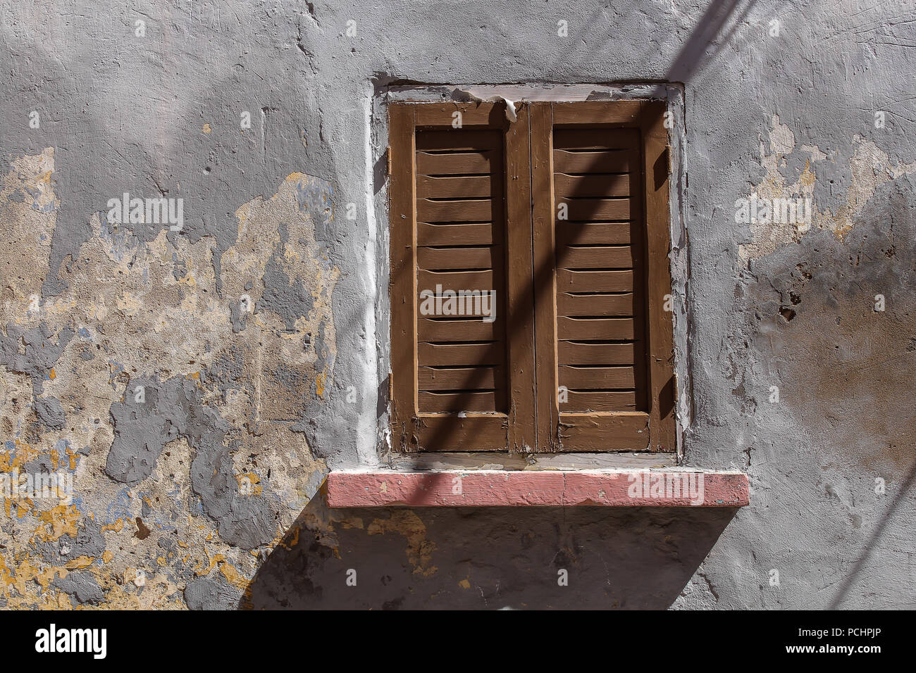 Couleur gris patiné de la façade d'une maison à El Jadida, Maroc. Fenêtre avec un obturateur fermé brun en bois. Les lignes d'ombre des câbles dans le stre Banque D'Images