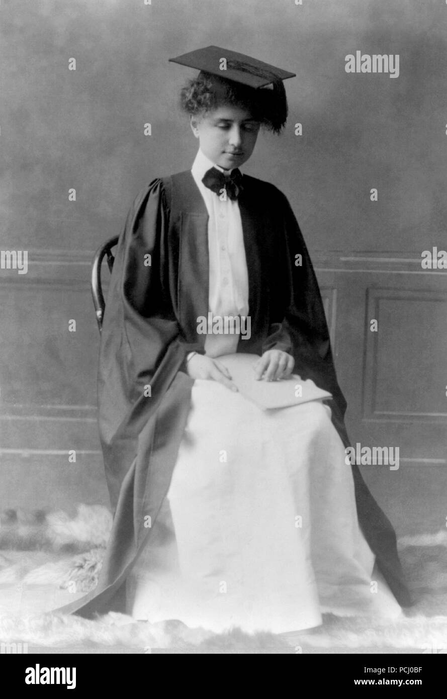 Helen Keller, portrait en pied assis wearing cap and gown et tenant un livre en braille, 11 janvier 1904. Helen Keller (27 juin 1880 - 1 juin 1968) était un écrivain, activiste politique, et conférencier. Elle a été la première personne atteinte de surdi-cécité à gagner d'un baccalauréat. Banque D'Images