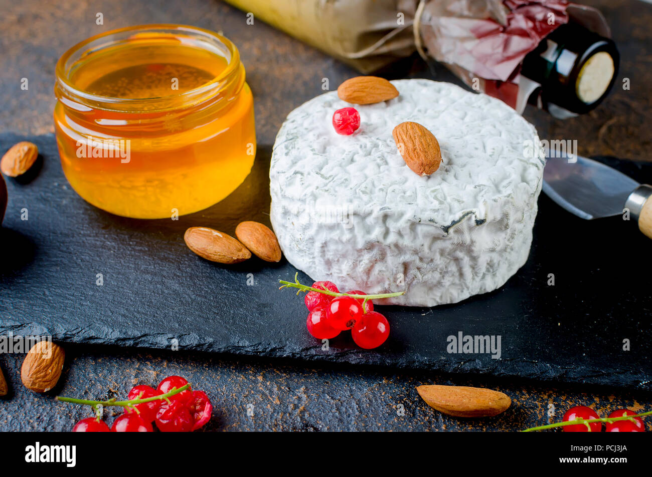 Tête ronde de fromage bleu avec du miel, de cassis, de fruits à coque et une bouteille de vin sur un tableau sombre, concept de gastronomie, fromage italien, romantique ev Banque D'Images