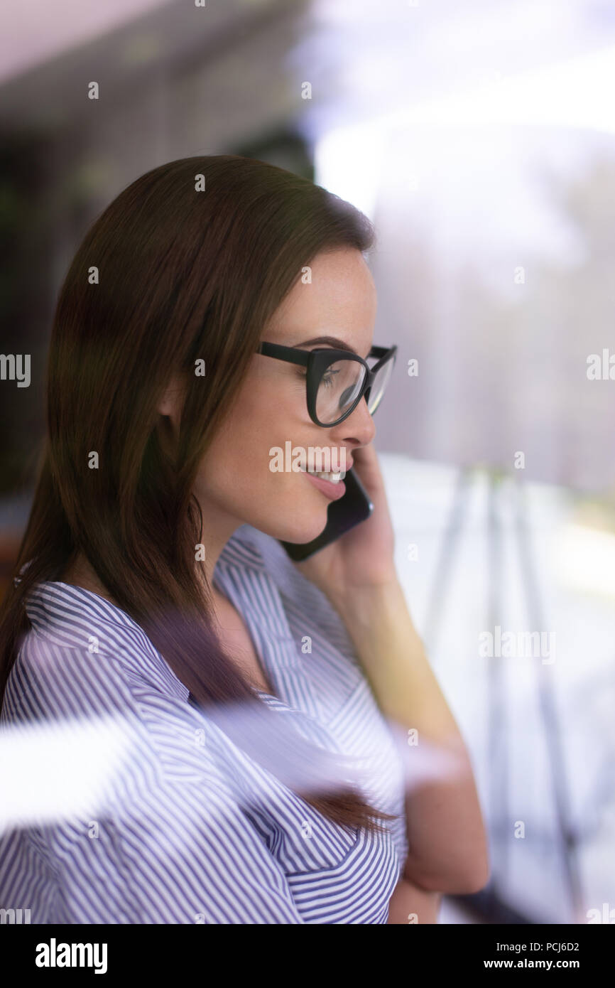 Jeune femme intelligente appelant derrière une vitre Banque D'Images