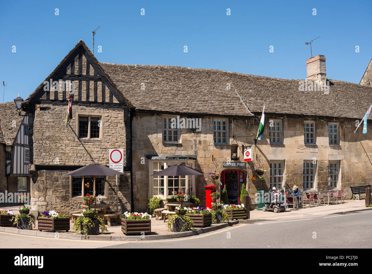 Les gens assis à l'extérieur de la poste Café, café et cake maker shop, Place du marché, Fairford, Gloucestershire, Royaume-Uni Banque D'Images