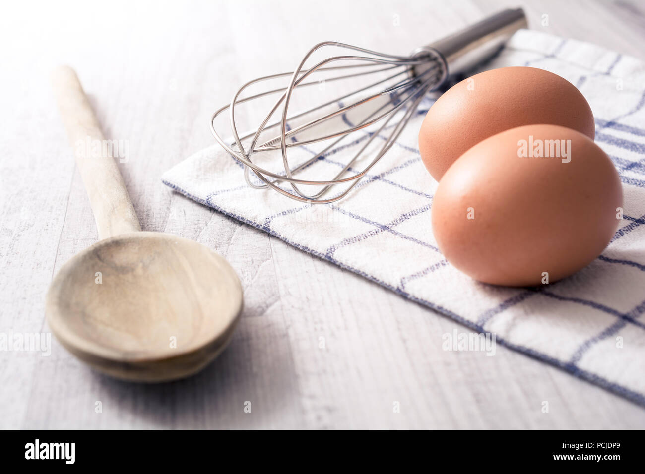 Préparer le petit déjeuner Œufs Concept avec 2 Œufs, une cuillère en bois, un batteur à oeufs et d'une serviette sur une table de cuisine Banque D'Images