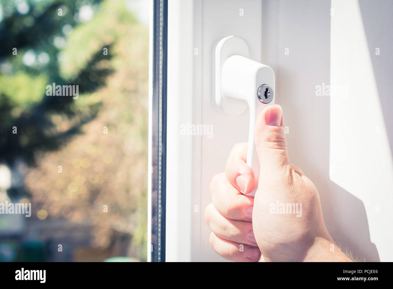Homme main tenant une poignée de fenêtre verrouillable d'une fermeture de fenêtre blanche avec arbres en arrière-plan, prévenir les cambriolages Concept Banque D'Images