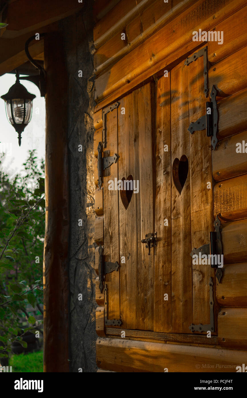 Volets en bois en forme de coeur avec des coupes. Vieille fenêtre avec charnières en fer sur mountain cabin. Banque D'Images