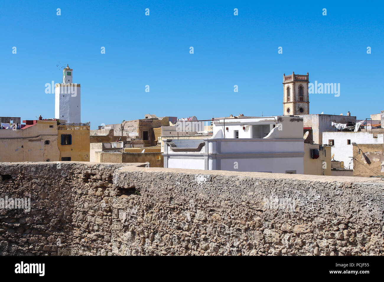 Toits et murs de l'immeuble d'habitations et sur la gauche une tour de grande mosquée de ancienne forteresse portugaise à El Jadida, Maroc. Ciel bleu Banque D'Images