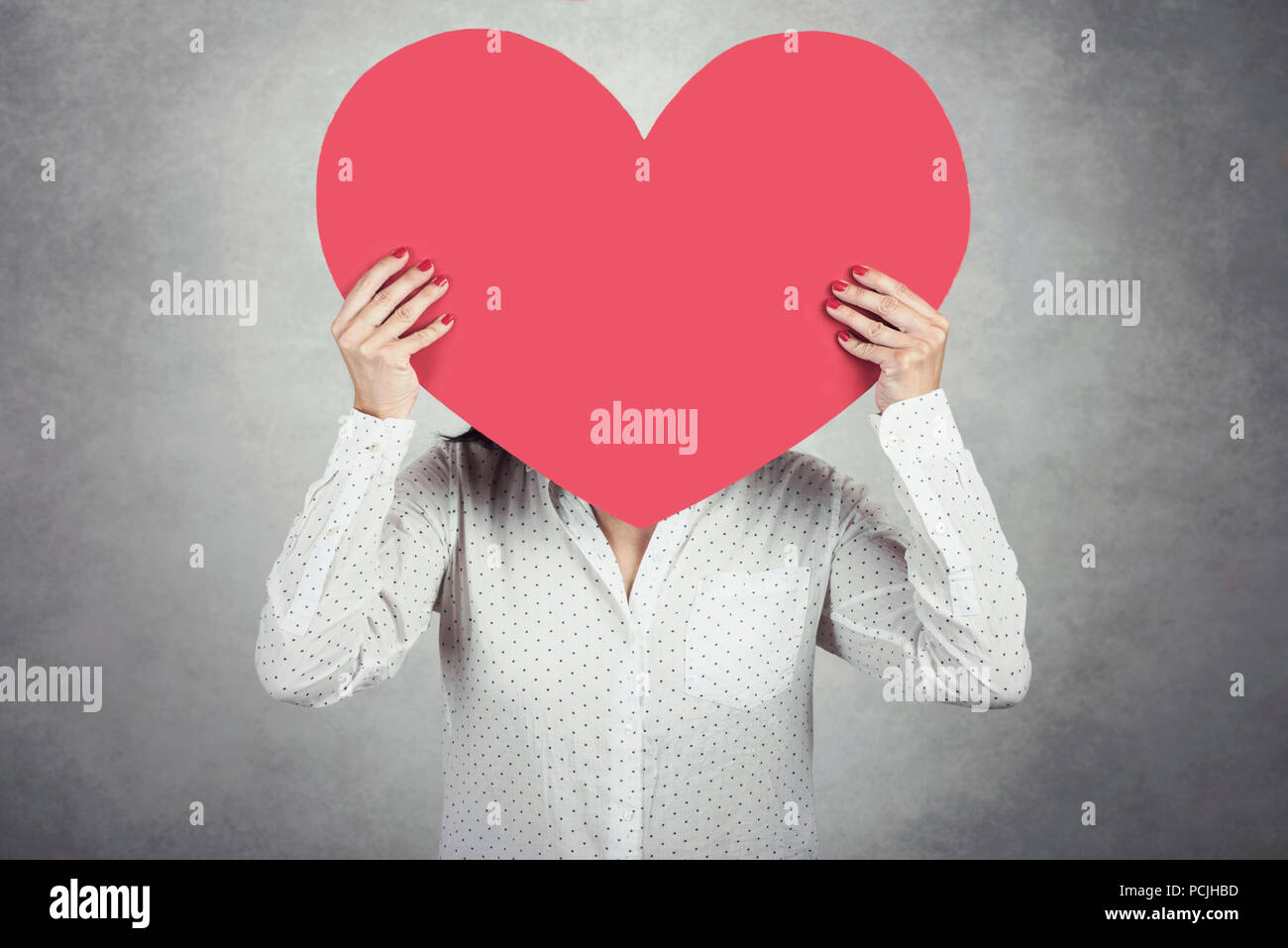 Young Woman holding cœur rouge sur fond gris Banque D'Images