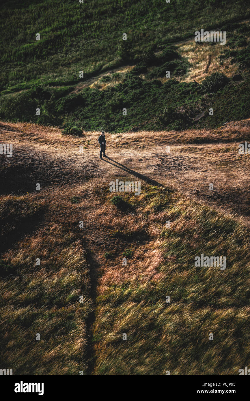 Randonneur sur le sentier de Holyrood Park, Salisbury Crags et Arthur's Seat au coucher du soleil. Edinburgh, Ecosse, Royaume-Uni. Banque D'Images