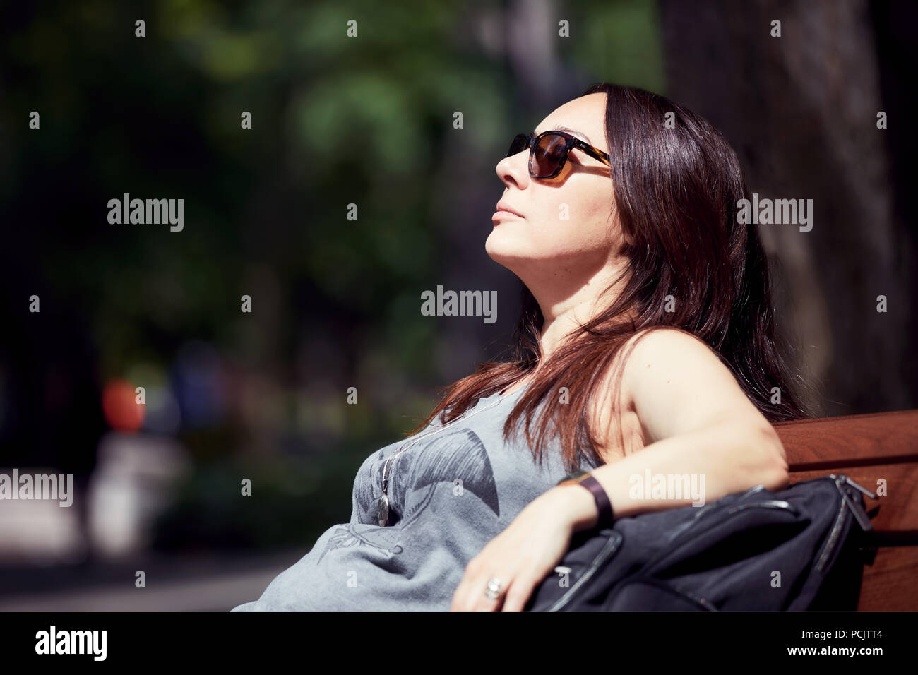 Femme rousse au soleil dans le parc. Elle porte des lunettes de soleil et  assis sur le banc Photo Stock - Alamy