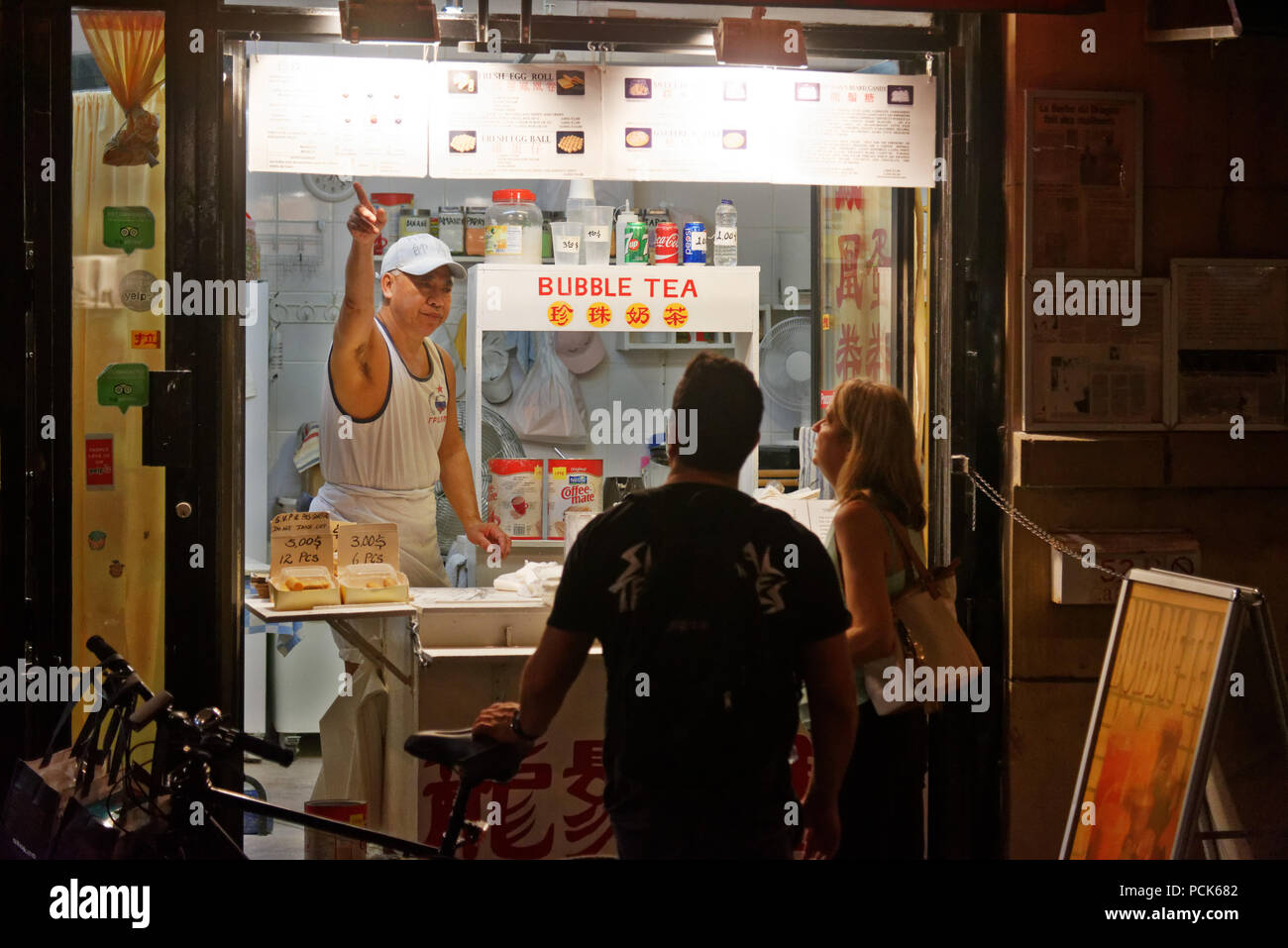 Un kiosque d'alimentation de rue chinois propriétaire montrant son menu à deux clients dans le quartier chinois de Montréal sur la Rue de la Gauchetière Banque D'Images