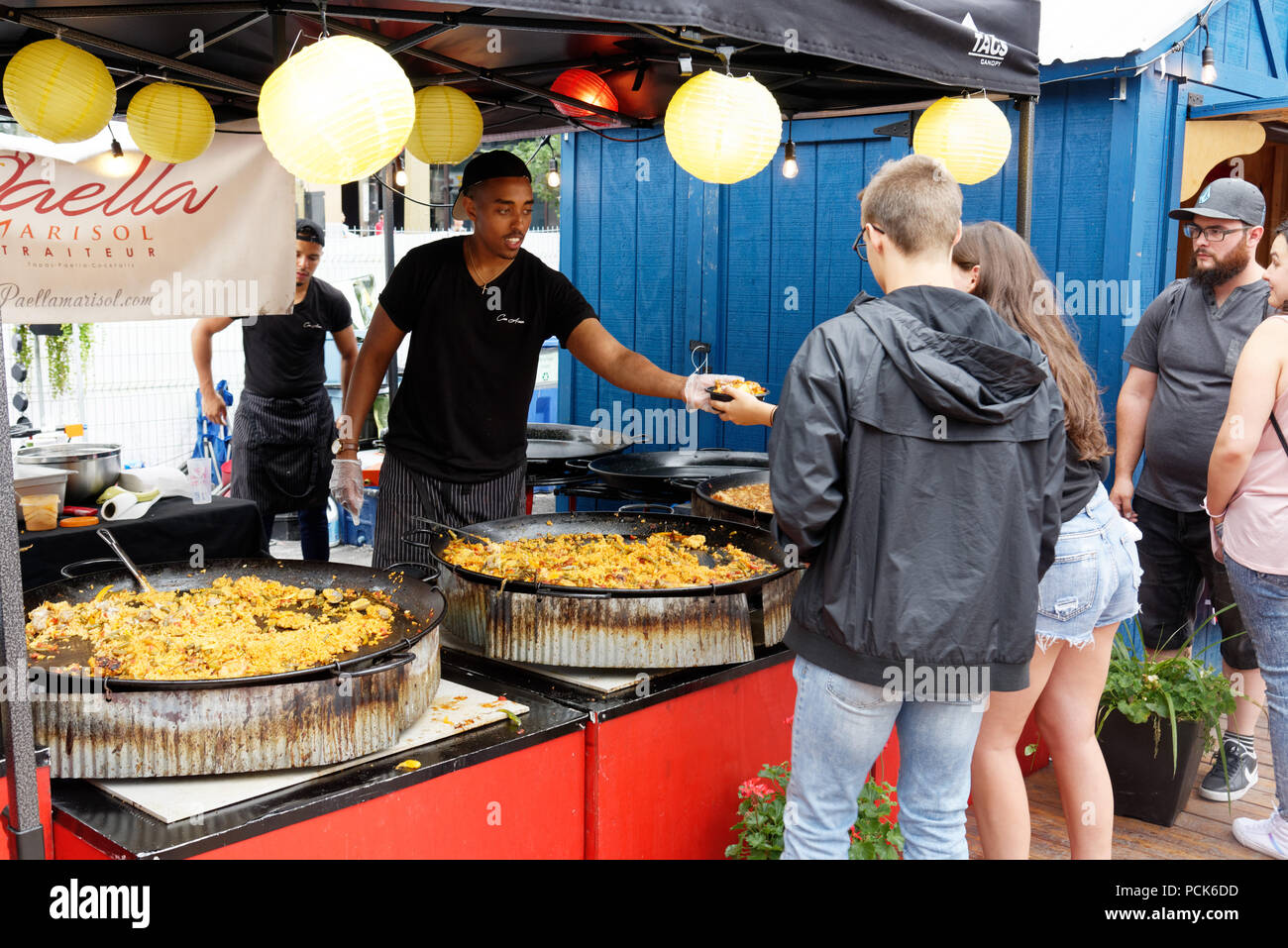 Un jeune homme au service de la paella à une dame à un client de l'alimentation de rue en plein air kiosque à Montréal Bouffons Banque D'Images