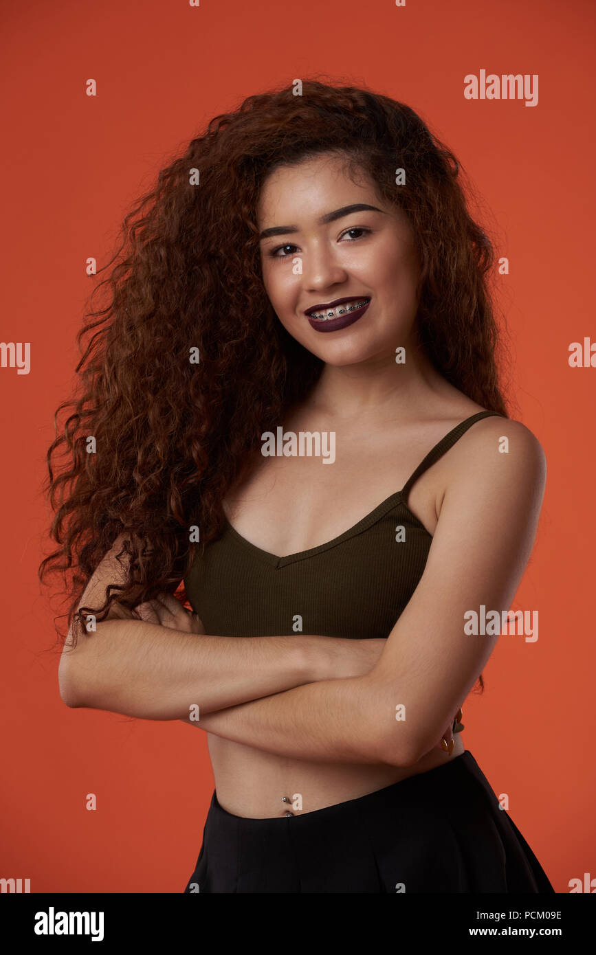 Smiling adolescent avec accolades portrait sur fond de couleur orange studio Banque D'Images