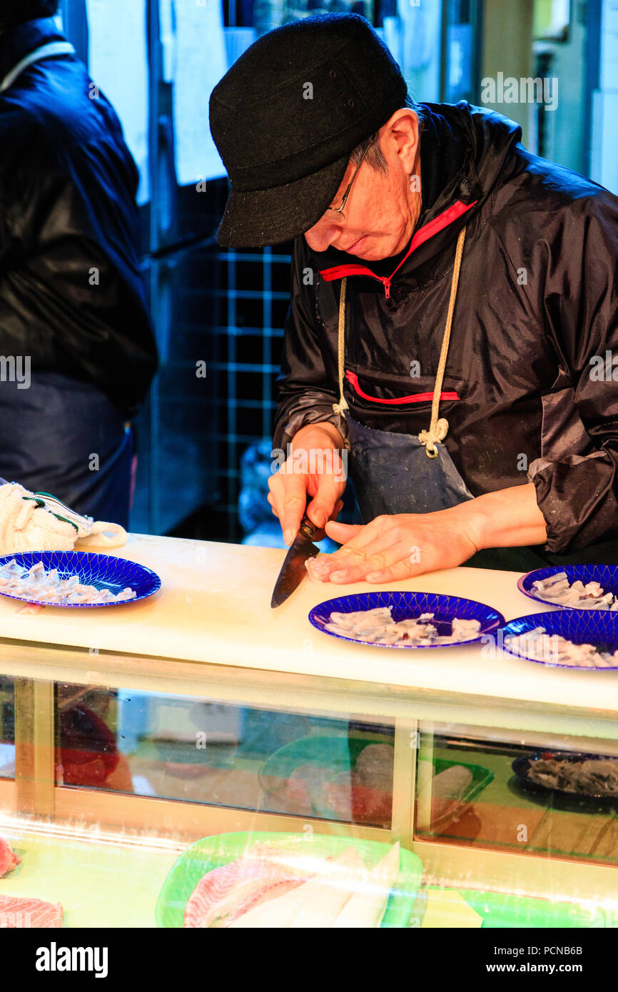 Kuromon Ichiba, Osaka's kitchen marché alimentaire. L'homme japonais, du découpage de petits morceaux de filet de poisson, avec quatre plaques bleues de couper le poisson sur la table Banque D'Images