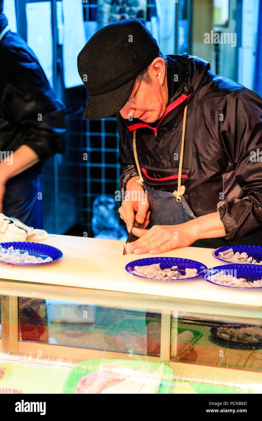 Kuromon Ichiba, Osaka's kitchen marché alimentaire. L'homme japonais, du découpage de petits morceaux de filet de poisson, avec quatre plaques bleues de couper le poisson sur la table Banque D'Images