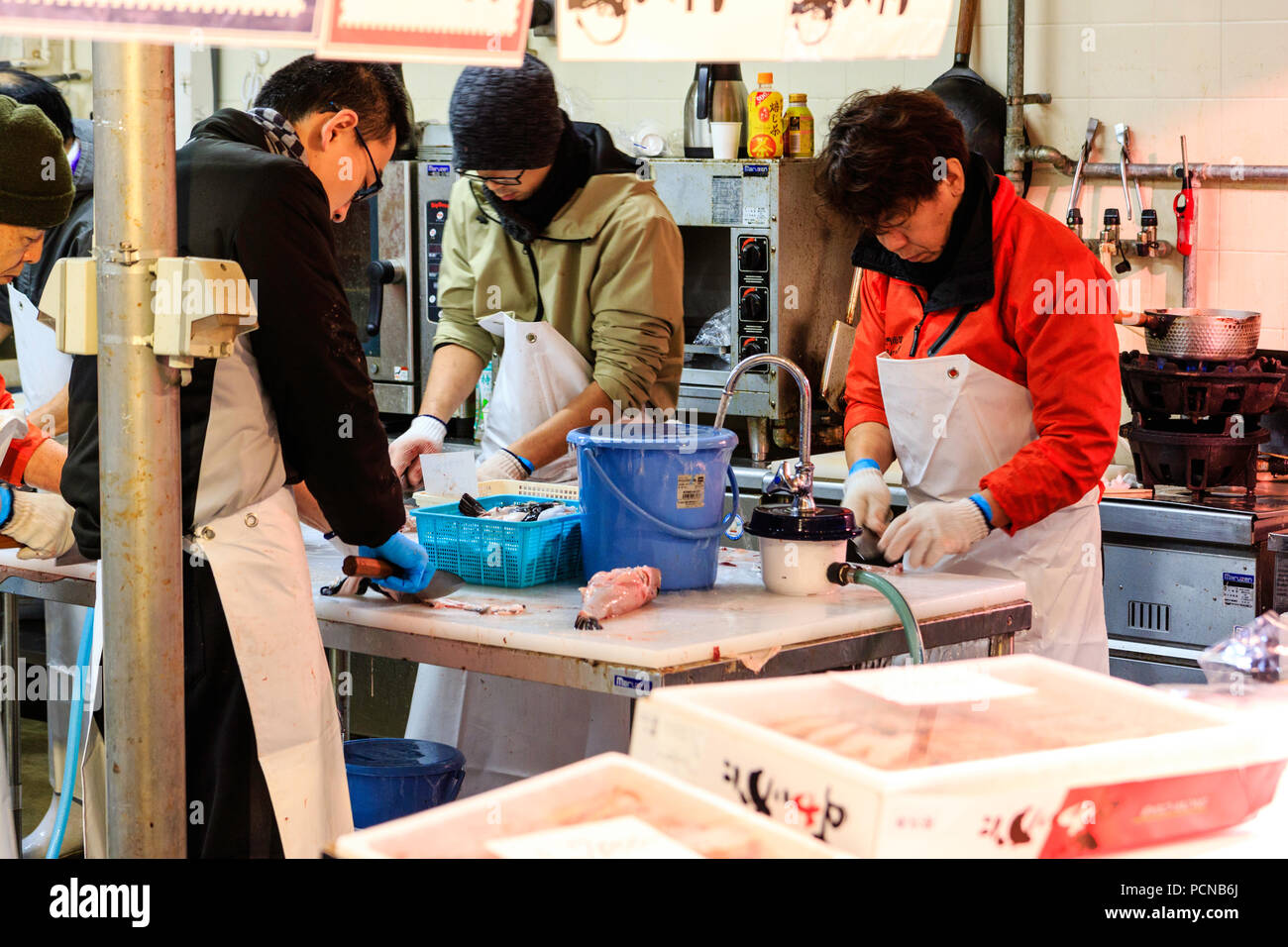 Kuromon Ichiba, Osaka's kitchen marché alimentaire. Quatre hommes, debout alors que le tranchage poissons jusqu', travaillant sur la table avec de l'eau qui coule au large de l'extrémité. Banque D'Images