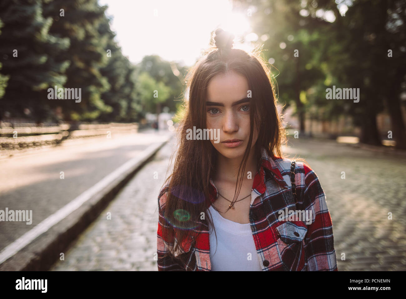 Portrait de superbe jeune femme avec calme en face de la lumière du soleil. Teen girl wearing plaid shirt rouge debout sur l'pavée à Banque D'Images