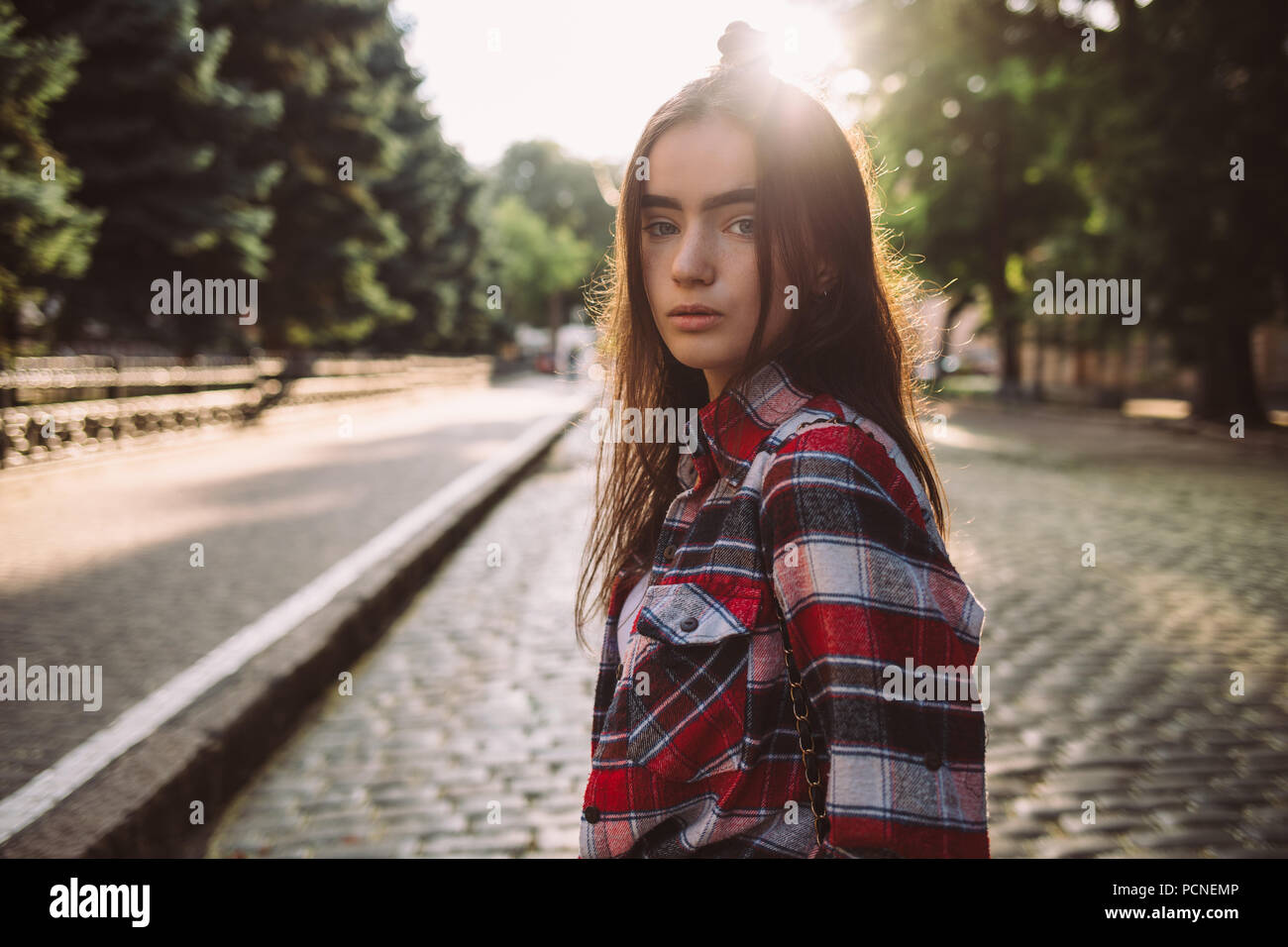 Teen girl wearing plaid shirt debout en marchant autour de la ville européenne avec une rue pavée. Portrait de la belle jeune femme avec le visage calme Banque D'Images