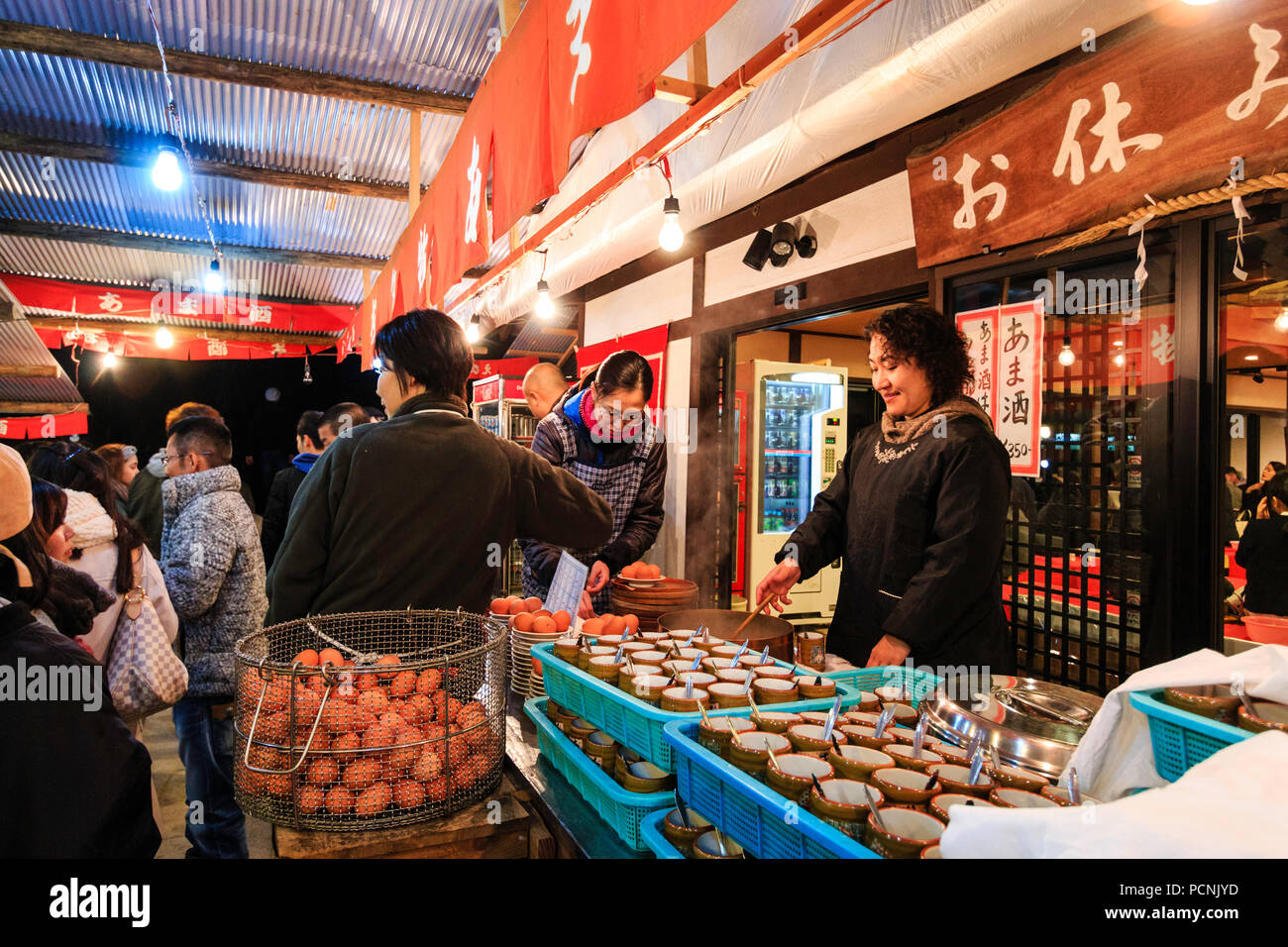 Shogatsu, nouvel an à Nishinomiya culte, le Japon. Réchauffement de la femme oeufs dans le grand bol d'eau bouillante, les plateaux de tasses et de cuillères en premier plan. Banque D'Images