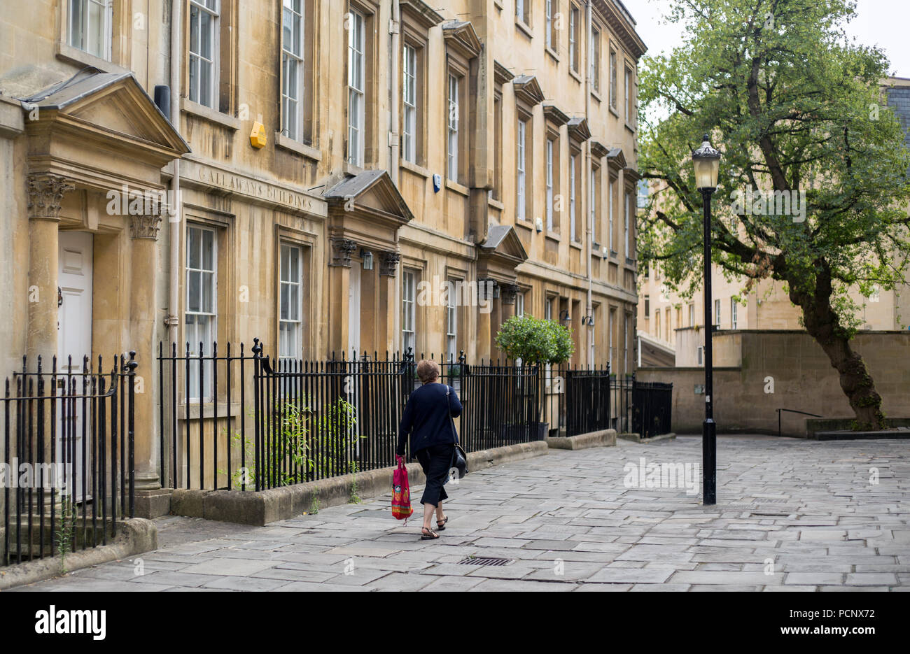 Une femme porte un sac shopping rouge le long d'une terrasse de maisons de ville géorgiennes à Bath. Banque D'Images