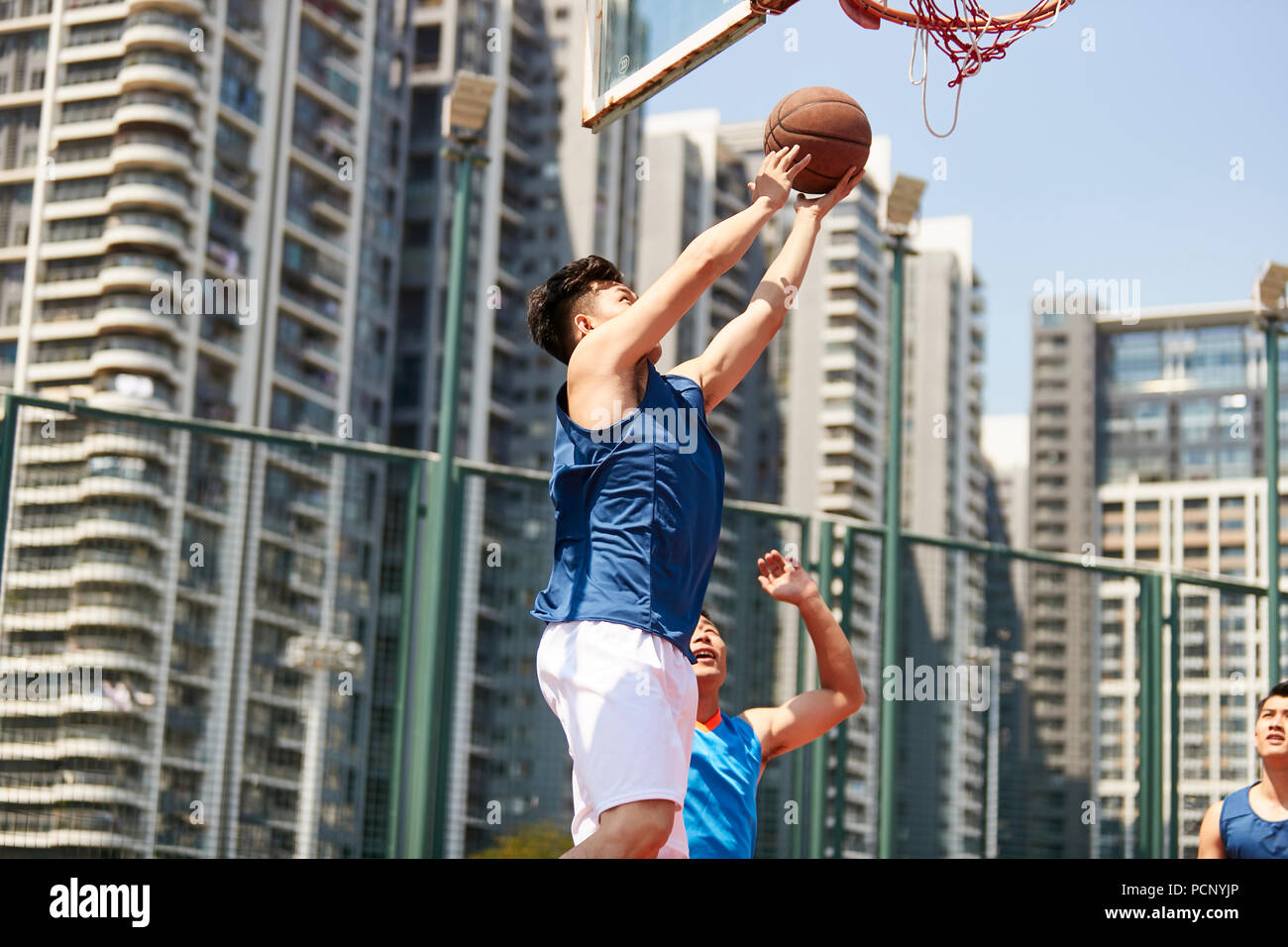 Jeune joueur de basket-ball de l'Asie à la hausse pour un layup tout en adversaire de jouer la défense. Banque D'Images