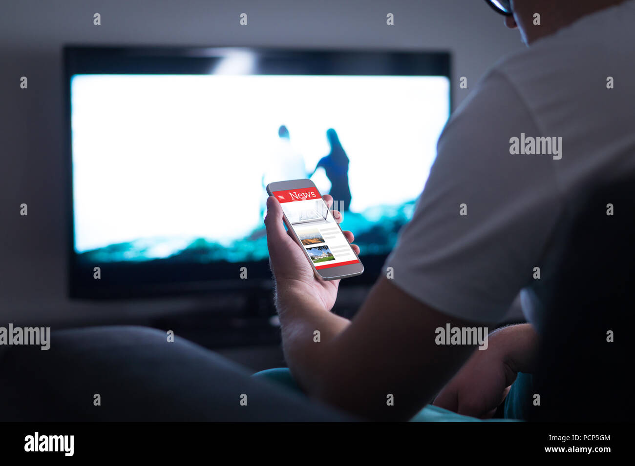 La lecture de l'homme en ligne nouvelles sur smartphone à la maison. Actualité mobile site web, une application ou un portail sur l'écran du téléphone cellulaire. La tenue en main smart device. Banque D'Images