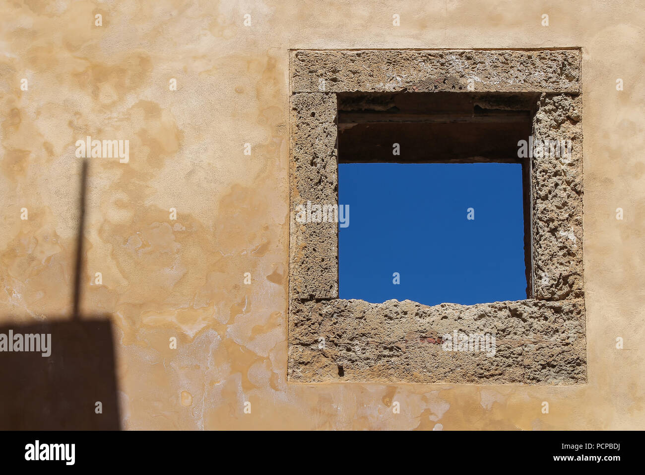 Mur avec une structure et une ombre façade vieillies. La place traditionnelle fenêtre avec un bâti en pierre. Ciel bleu. El Jadida, Maroc. Banque D'Images