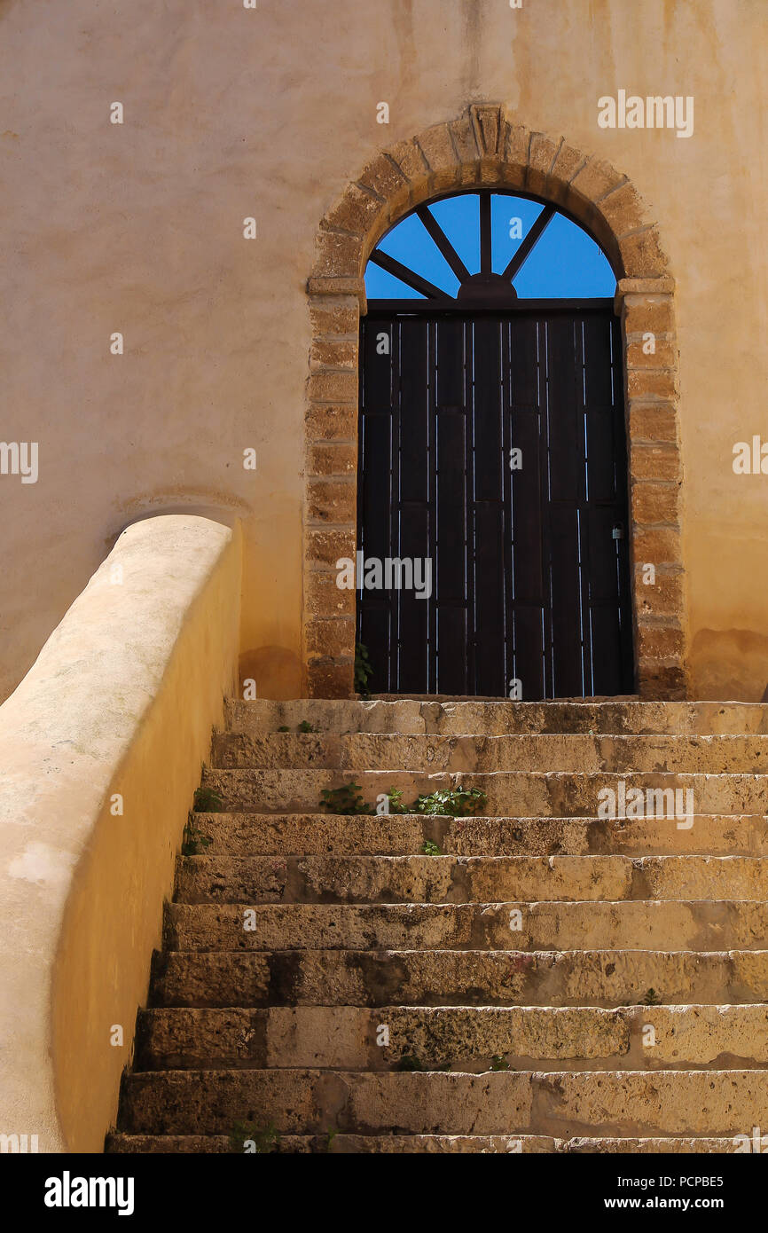 Escaliers en pierre à la porte en bois avec un arc. Arch avec des trous, où est visible un bleu ciel. Dans l'ancien bâtiment de la forteresse portugaise à El Jadida, Banque D'Images