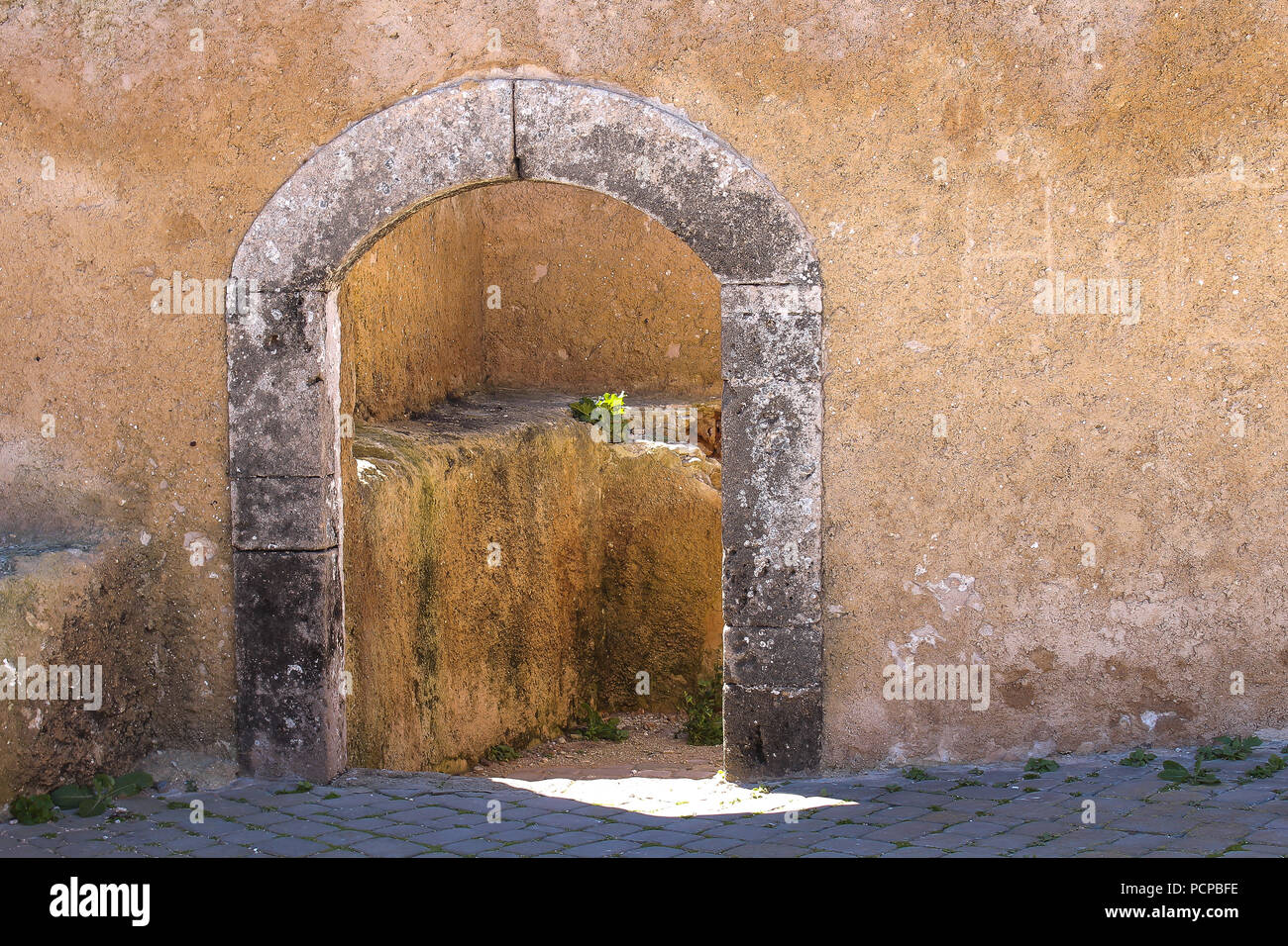 Façade structurée du mur avec une porte avec un arc en pierre et le châssis. Entrée d'une chambre à l'enrichissement d'El Jadida, Maroc. Banque D'Images