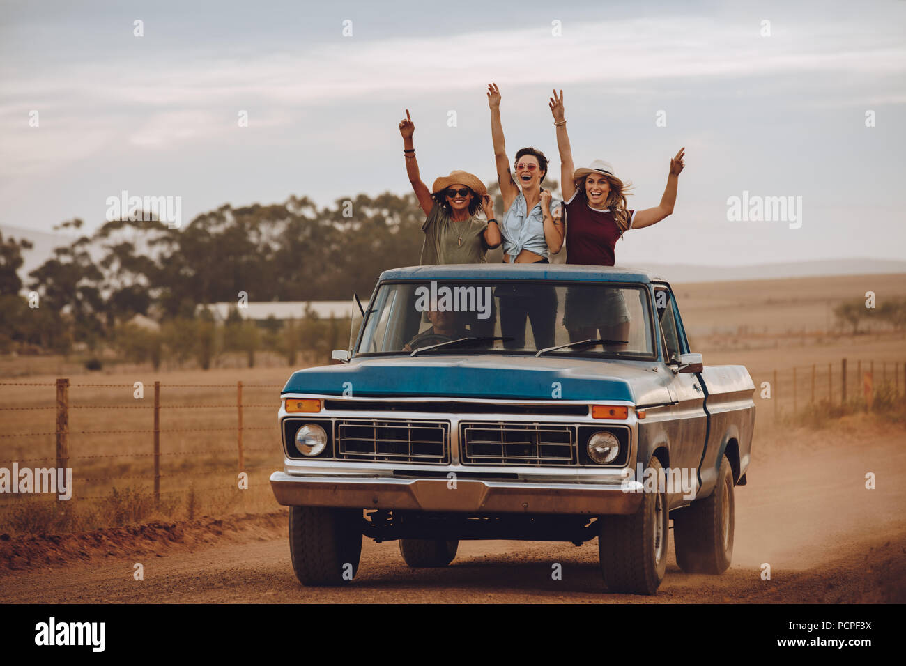 Trois femmes sur un roadtrip dans la campagne sur l'arrière d'une camionnette. Les amis debout dans l'arrière d'un camion ouvert rire avec leurs h Banque D'Images