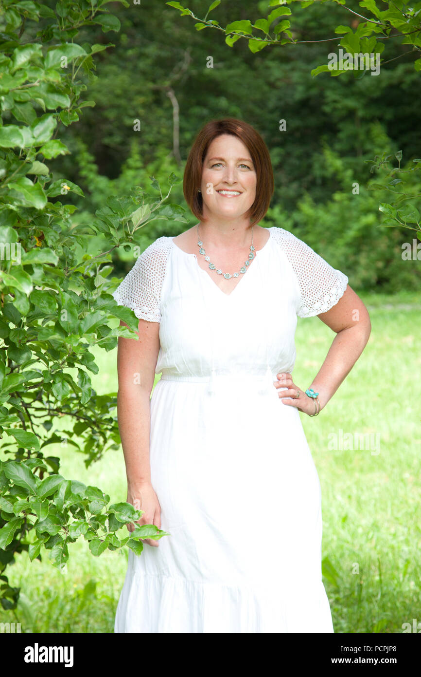 Une femme aux cheveux rouge se tient et sourires pour un joli portrait en robe blanche à l'extérieur Banque D'Images