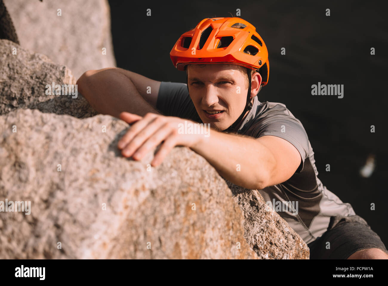 Beau jeune voyageur en casque d'escalade sur roche et looking at camera Banque D'Images