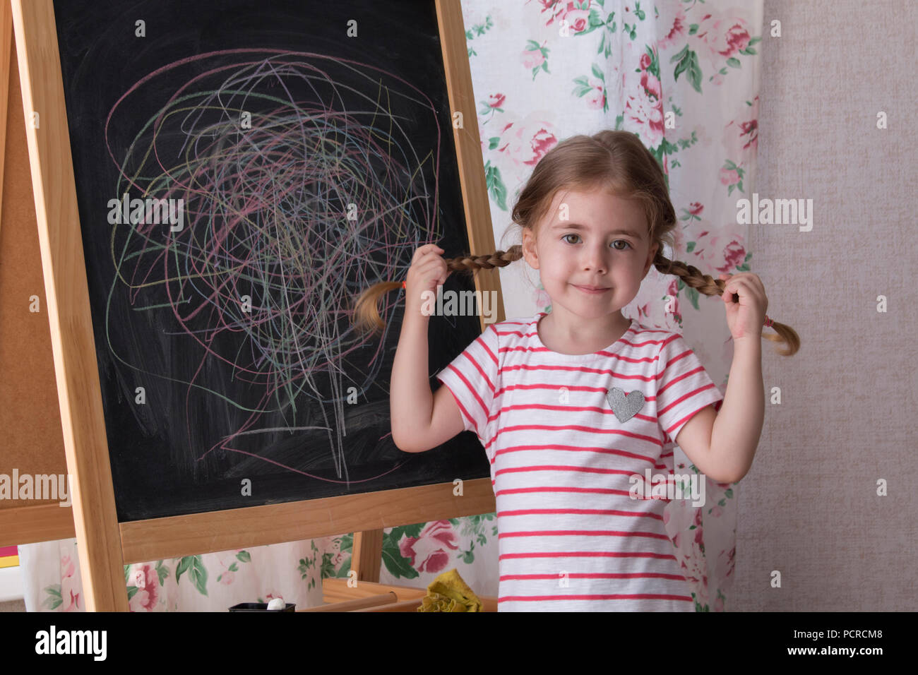 Dessin de l'enfant avec des morceaux de craie de couleur sur le tableau. La créativité et l'expression de jeune fille est à la recherche de l'appareil photo. Concept d'expression et d'apprentissage Banque D'Images