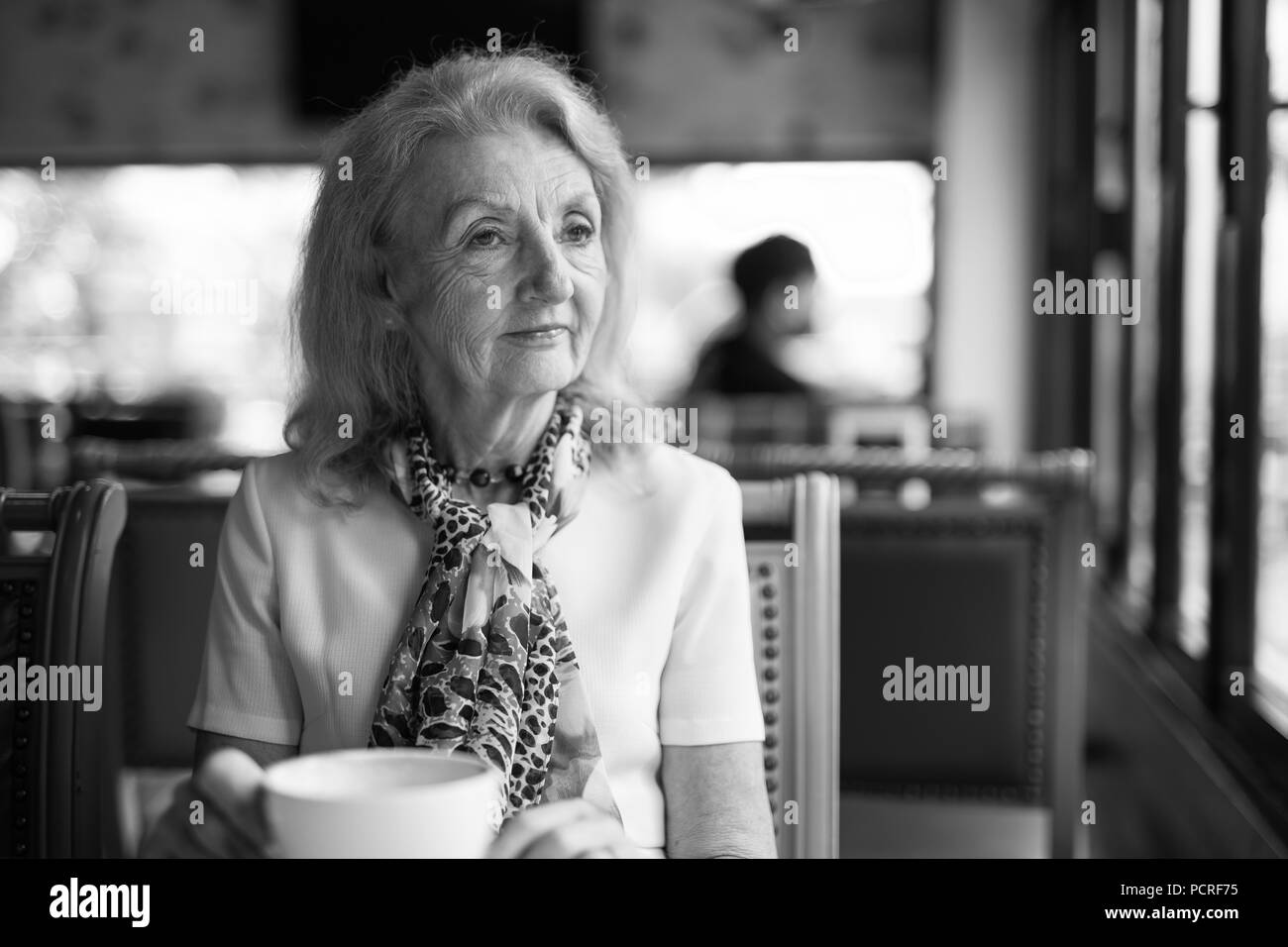 Le noir et blanc Portrait of Senior Woman boire du café et à la fenêtre de Banque D'Images