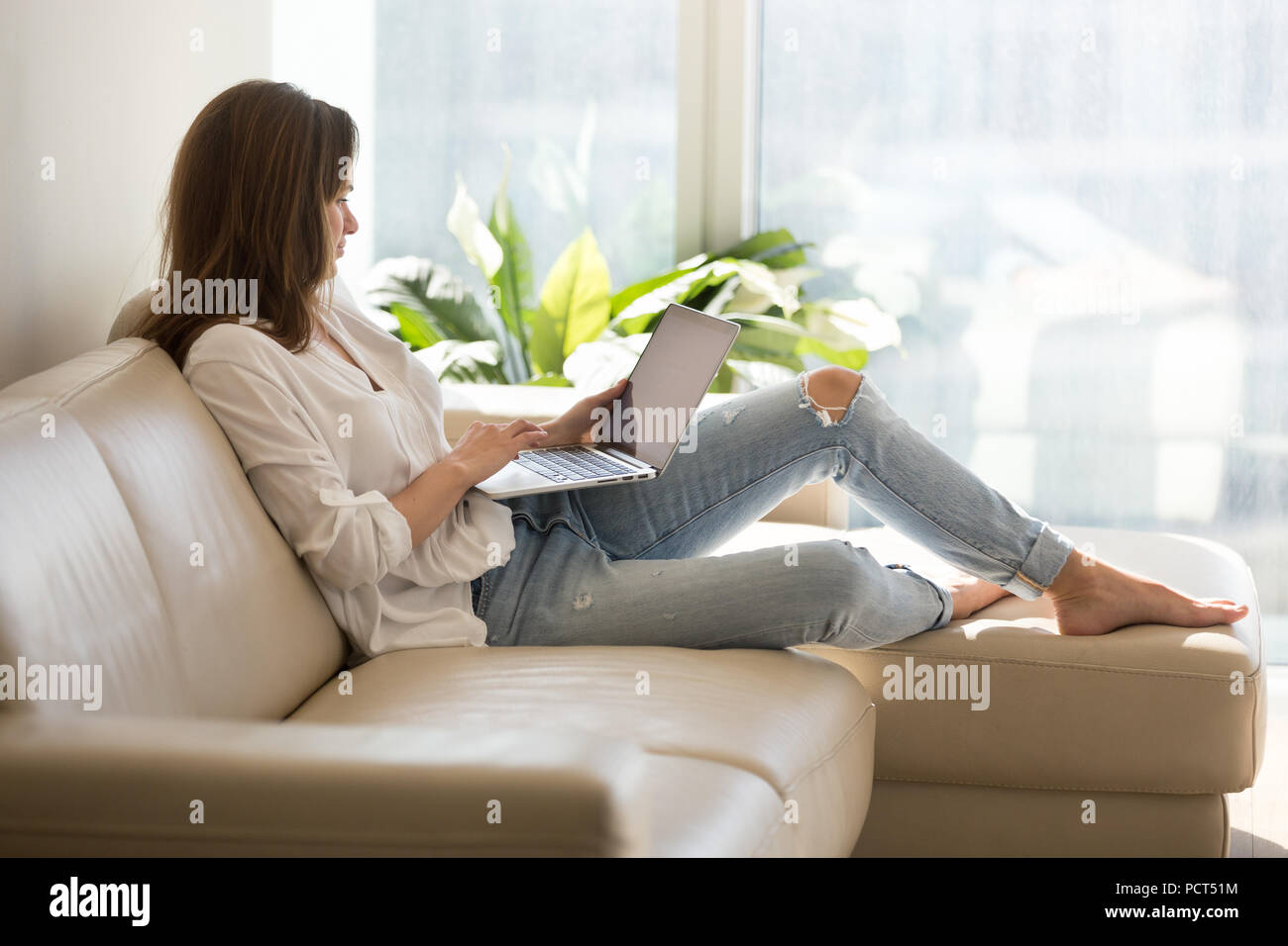 Happy female internet navigation sitting on sofa at home Banque D'Images