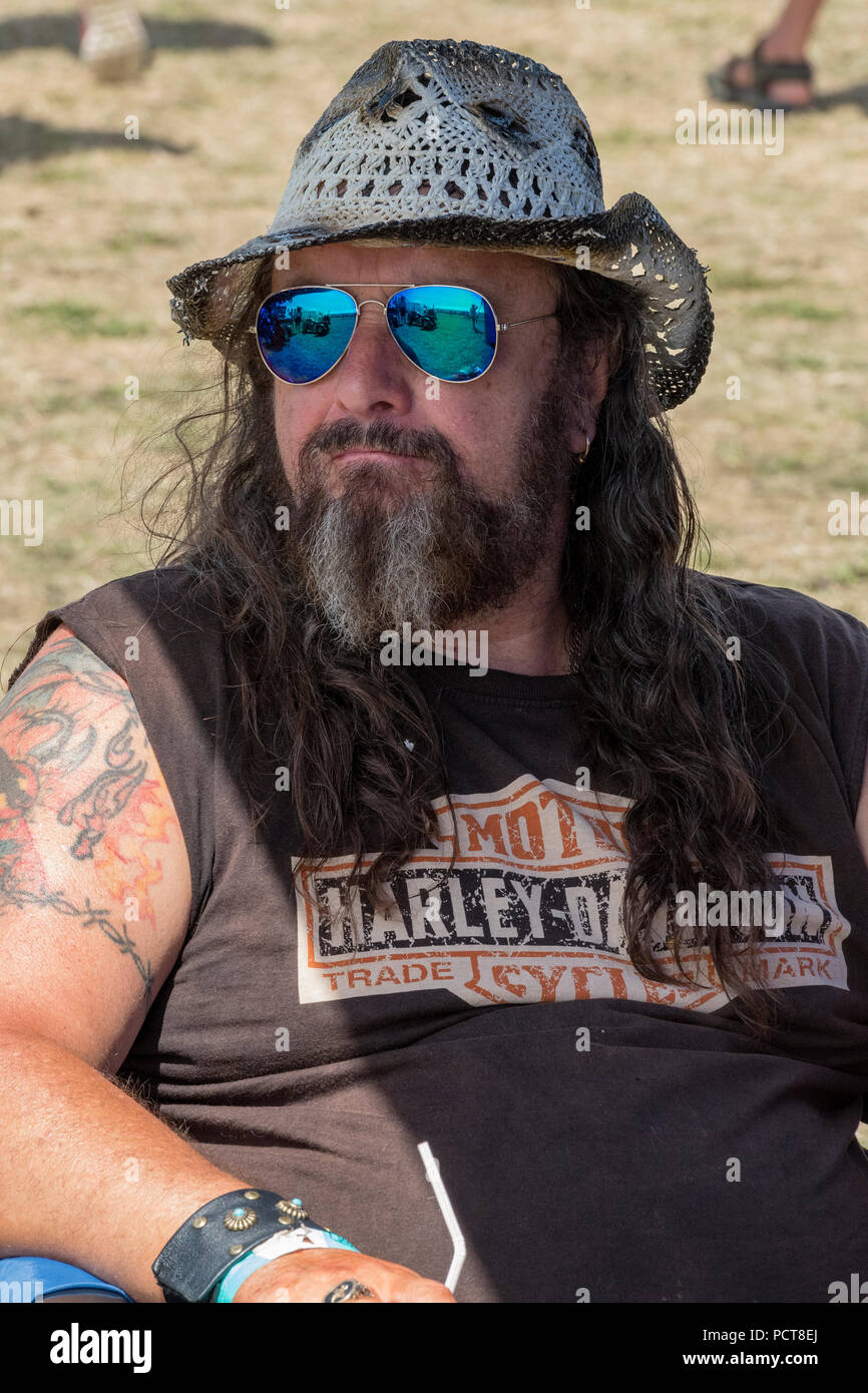 Un motard poilu avec une grande barbe longue et portant des lunettes de soleil un chapeau de cowboy. Tatouages et t-shirt Harley Davidson. Banque D'Images