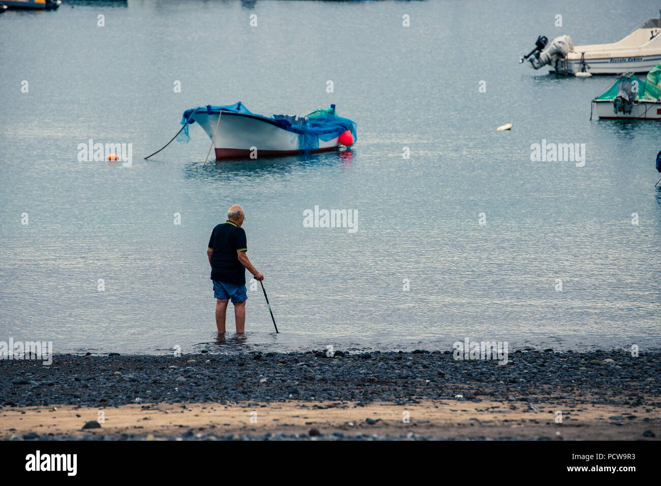 Vieil homme avec une canne, tremper ses pieds sur la côte de mer près de bateaux dans port. Banque D'Images