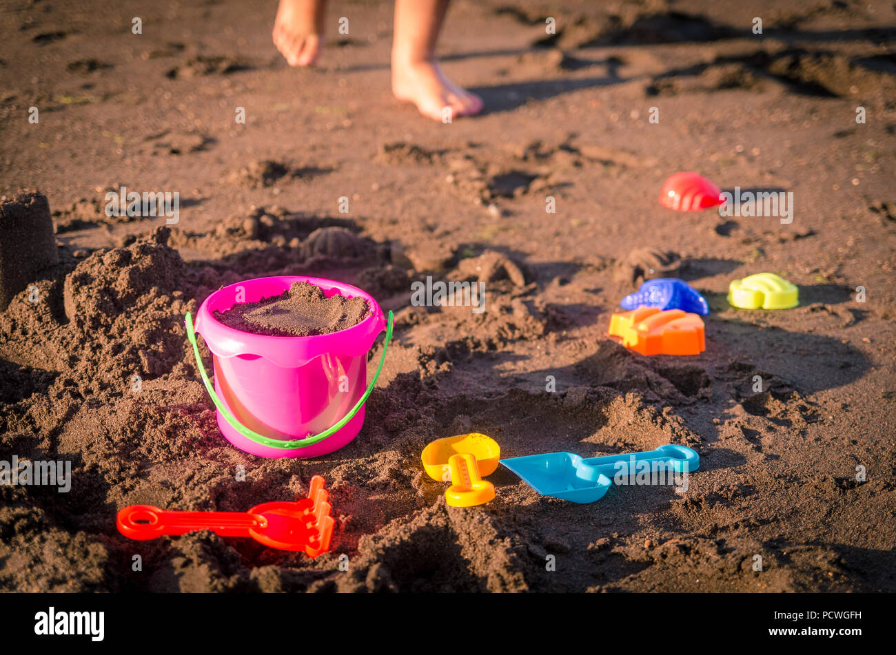 Les enfants des jouets de plage pour faire des châteaux de sable ou de sable située autour de chiffres dans le sable avec un kid's pieds visibles à marcher vers elle. Banque D'Images