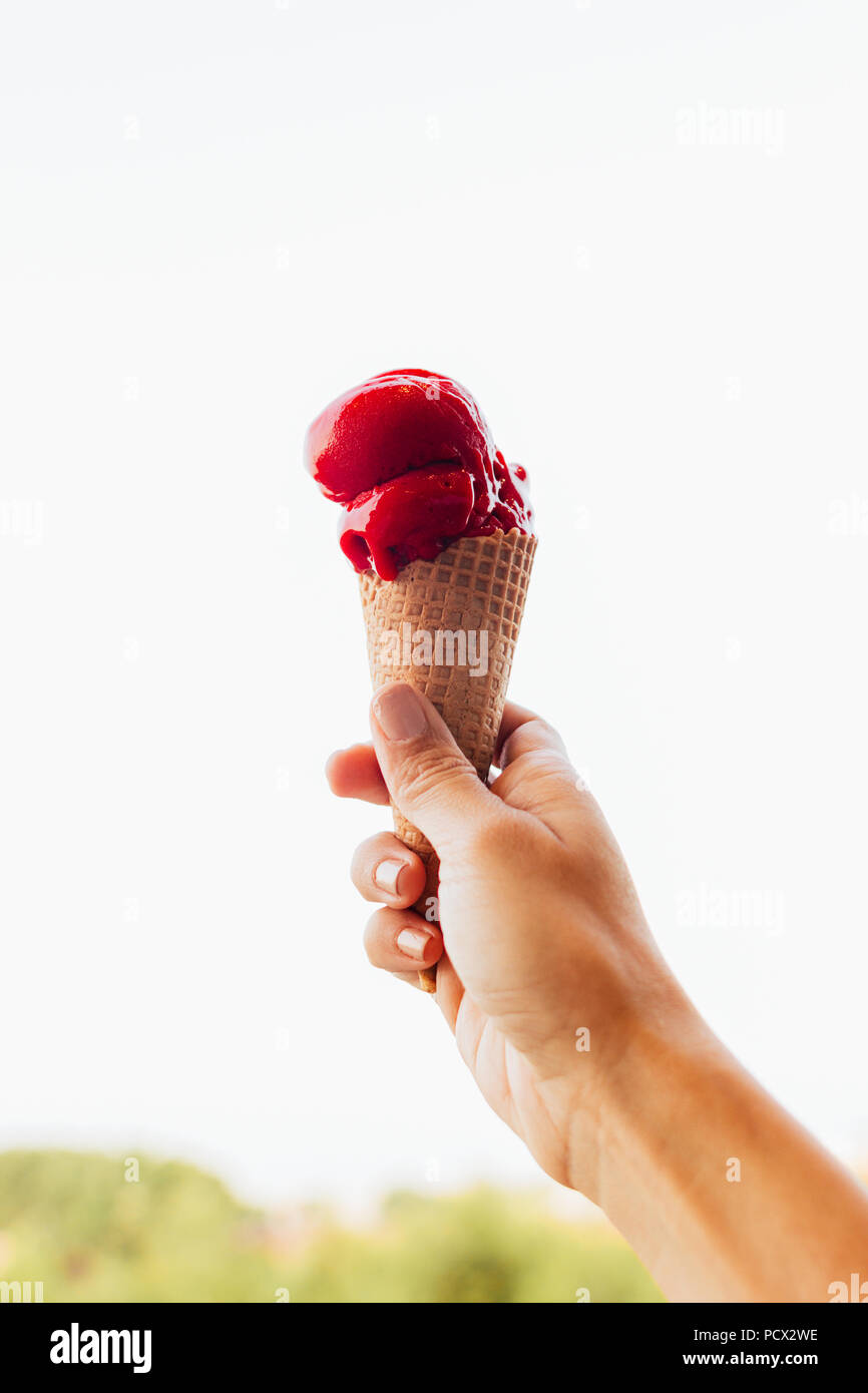 Woman's hand holding a jolie et appétissante de cône de glace à la framboise, la glace fond lentement dans la chaleur de l'été Banque D'Images