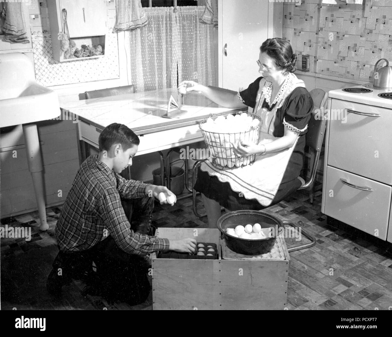 Femme d'agriculteurs dans la région de comté de Delaware, N.Y. pèse oeufs d'être commercialisés, afin qu'ils puissent être correctement évalué. Son fils de 11 ans, dans des endroits soigneusement la caisse les oeufs qui passent l'essai de pesage. 1941 Banque D'Images