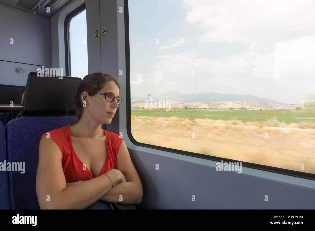 Une femme dans la vingtaine touristiques contempler d'une fenêtre de train au paysage grec chaud se précipiter sur la dernière ligne Thessaloniki-Larissa Banque D'Images