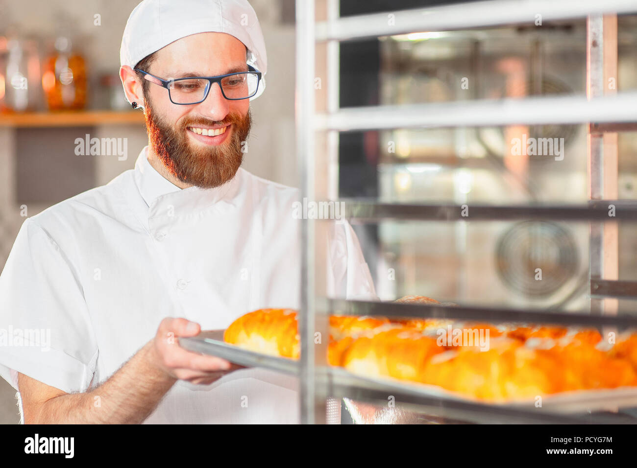 Un jeune beau baker sort chaude du four de cuisson dans la boulangerie. Banque D'Images