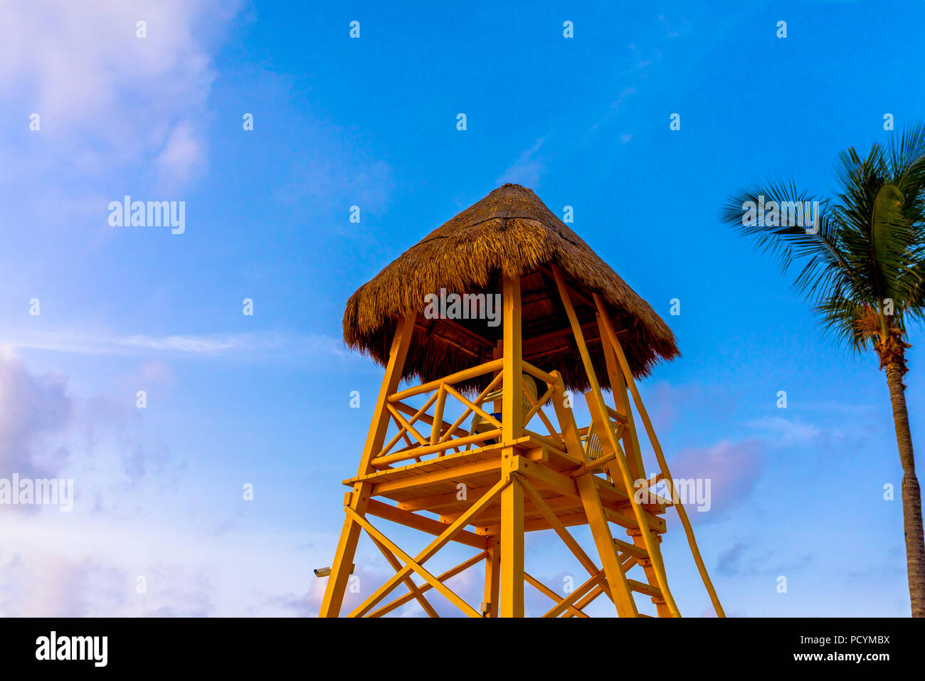 En bois et chaume jaune lifeguard tower ou la gare domine la mer des Caraïbes contre un ciel bleu tropicaux avec palmier Banque D'Images
