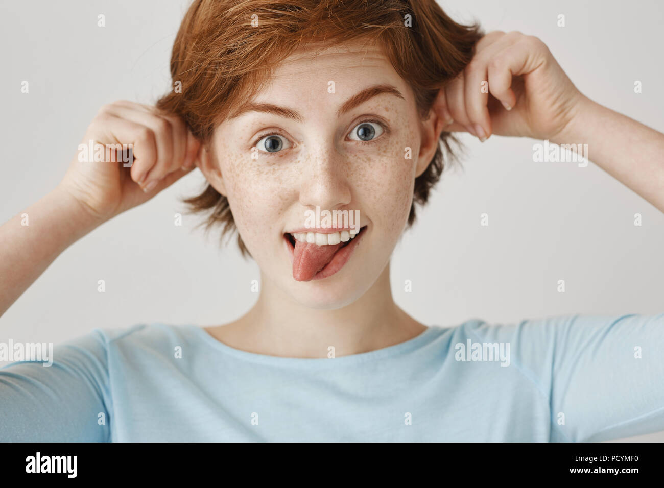 Close-up portrait of rousse enfantine joyeuse avec soeur adultes rousseur sticking out tongue et tirant les oreilles avec les mains, un large sourire tout en singeant o Banque D'Images