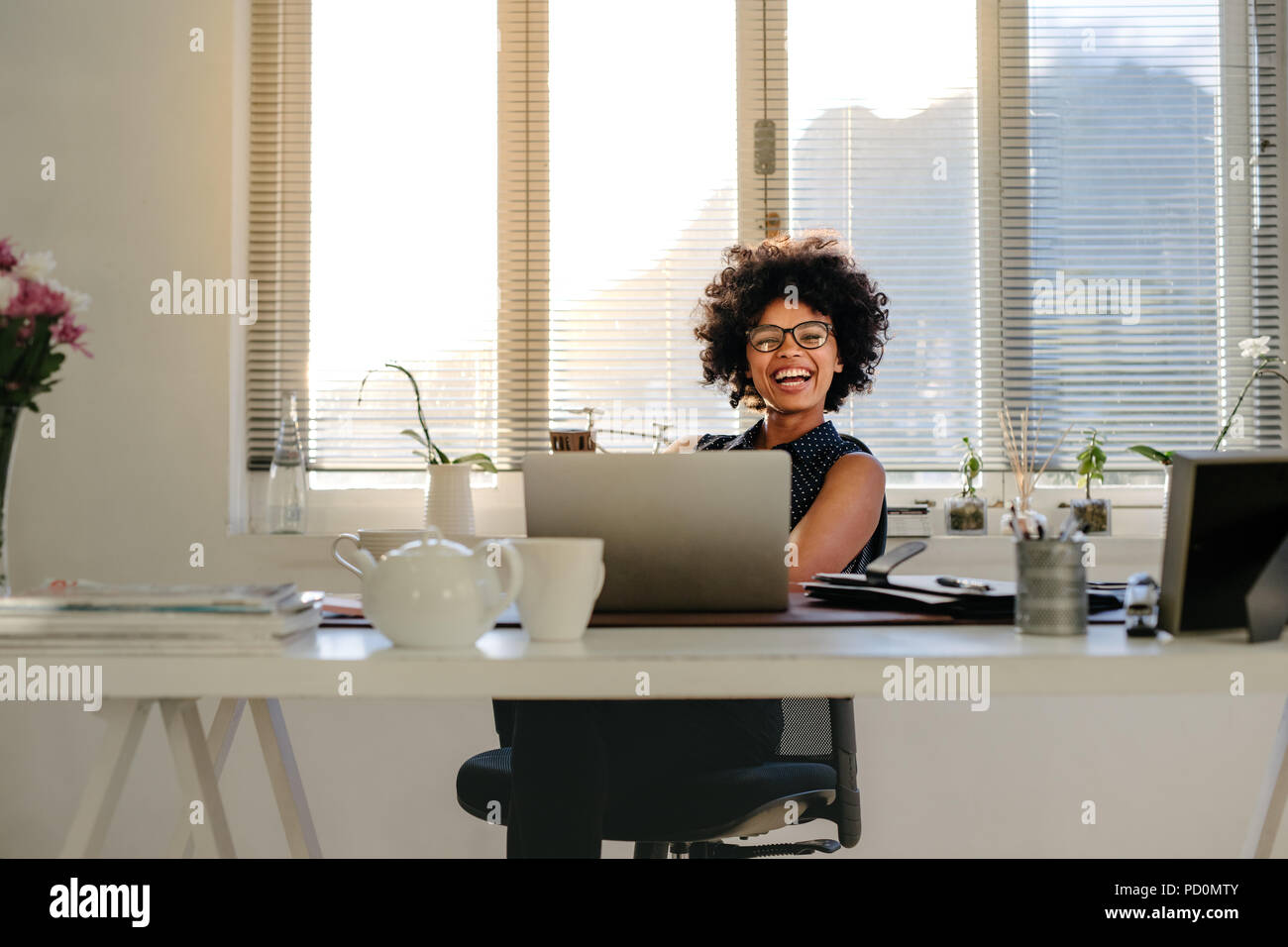 Portrait de belle jeune femme assise à son bureau et sourit. Happy african businesswoman in casuals dans Office. Banque D'Images